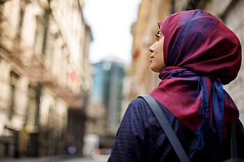 Portrait einer Frau mit buntem Kopftuch, die auf einer Straße steht.