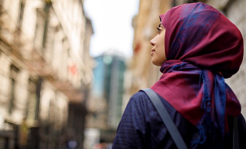 Portrait einer Frau mit buntem Kopftuch, die auf einer Straße steht.