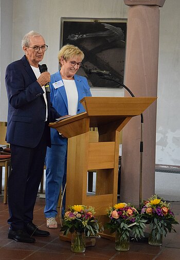 Mann mit Mikrophon und Frau hinter Stehpult