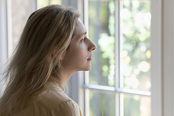 Frau blickt mit ernstem Blick aus Fenster