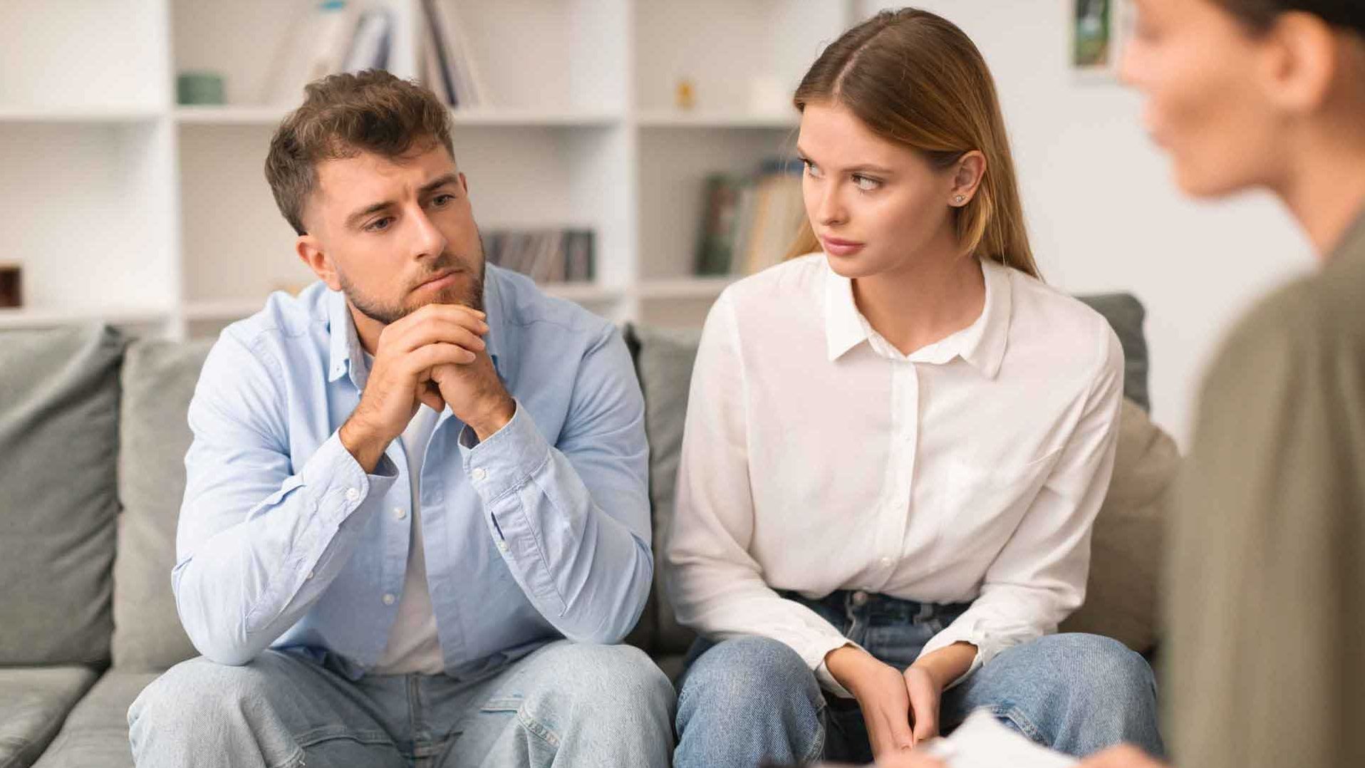 Zwei Erwachsene sitzen nebeneinander im Gespräch mit einer weiteren Person, die ihnen gegenübersitzt.