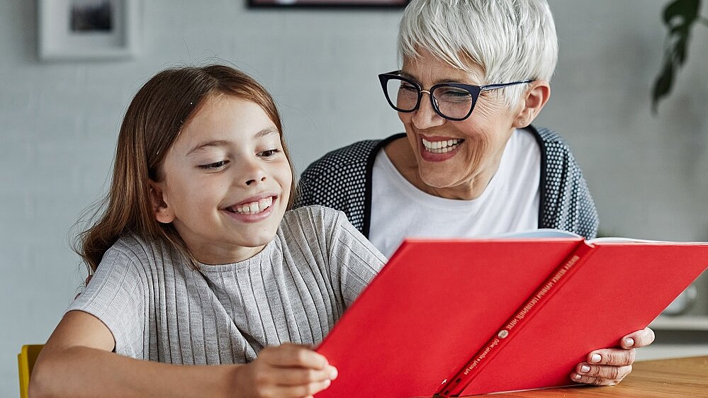 Schulkind und Seniorin schauen gemeinsam in Buch