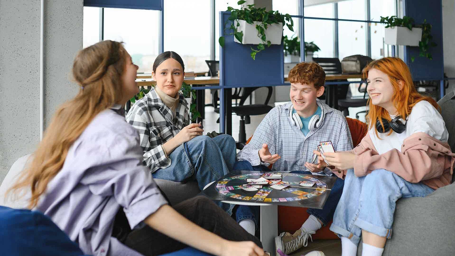 Vier Jugendliche sitzen in einem Kreis um einen Tisch und spielen ein Brettspiel