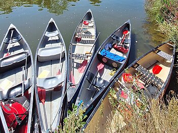 Fünf Kanus mit Gepäck liegen nebeneinander im Wasser.