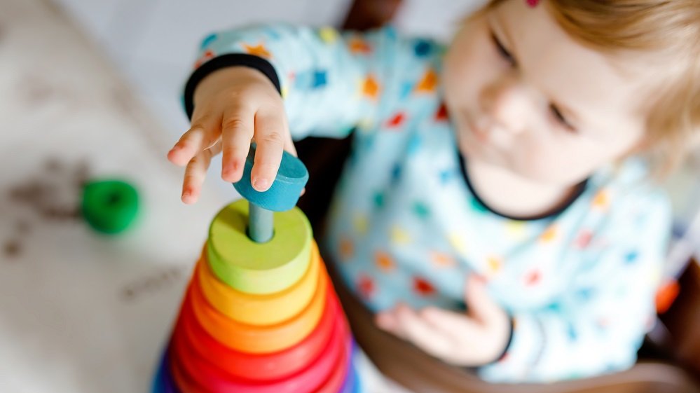 Kleinkind setzt bunte Holzringe als Turm aufeinander