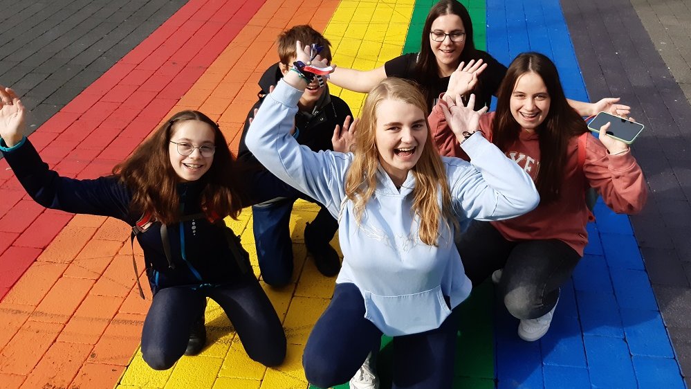 Gruppe von Jugendlichen knien auf aufgemaltem Regenbogen