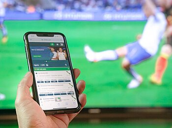 Handy mit Glücksspiel wird vor Fernsehgerät gehalten