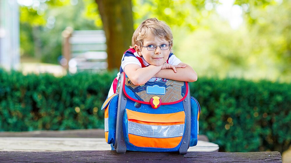 Junge stützt die Arme und seinen Kopf auf einen Schulranzen