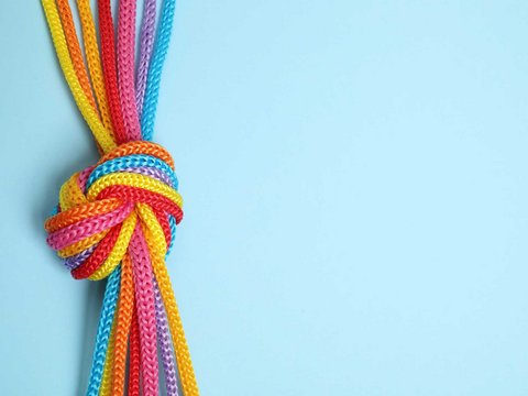 Mehrfarbige Kordeln sind zu einem Knoten verbunden als Symbol für Kooperation und Vernetzung