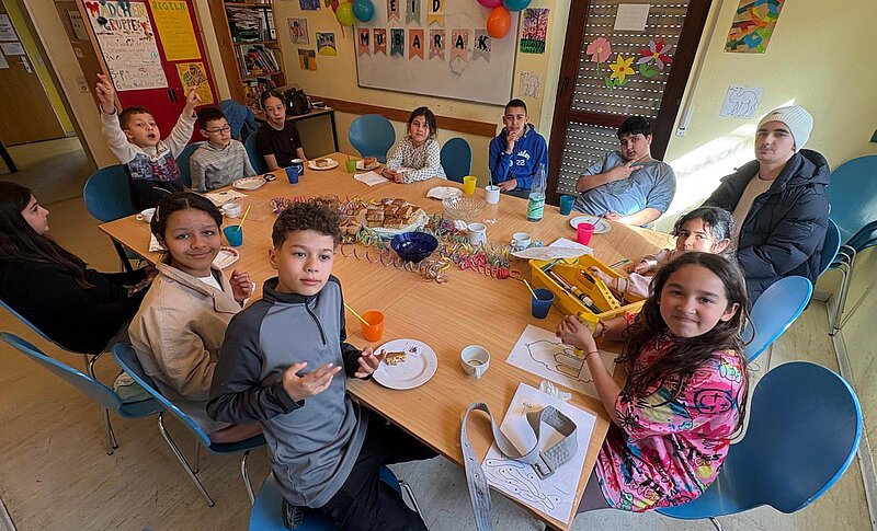 Kinder und Betreuer:innen sitzen um Tisch herum in geschmückten Raum