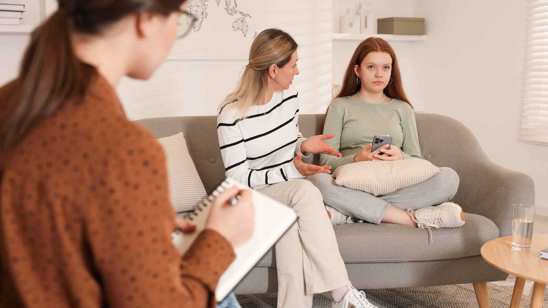 Eine Jugendliche und eine erwachsene Person im Austausch. Gegenüber sitzt eine weitere Person mit Schreibunterlagen.