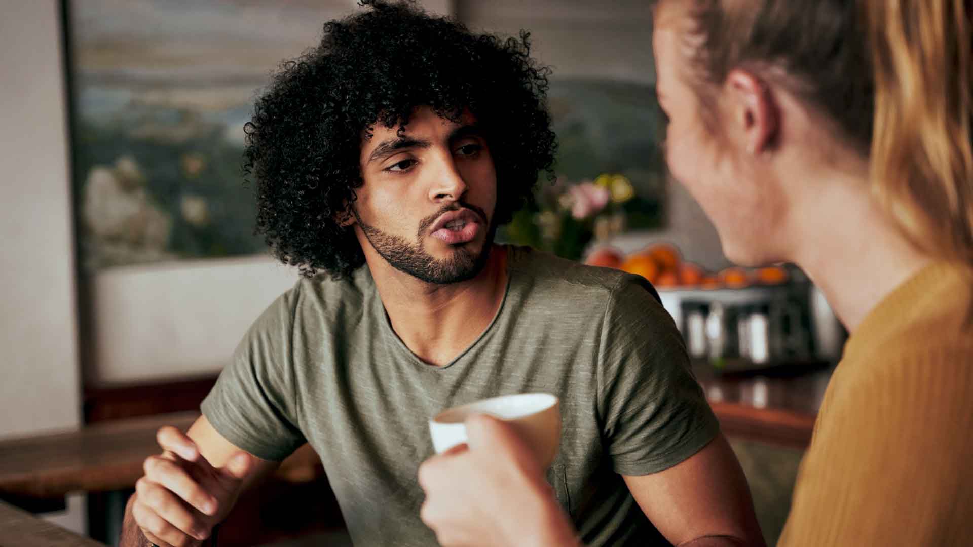 Nahaufnahme eines Dialogs an einem Tisch, mit Fokus auf eine sprechende Person und die zuhörende Person gegenüber.