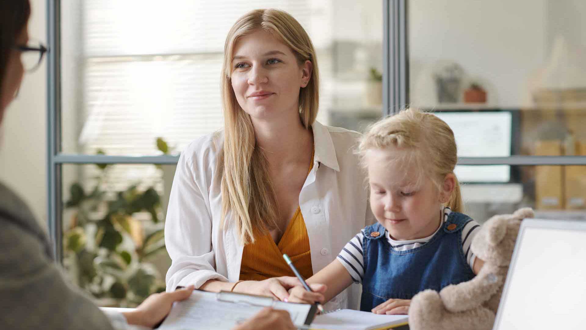 Eine Frau und ein Kind sitzen gemeinsam an einem Tisch im Gespräch mit einer weiteren Person.